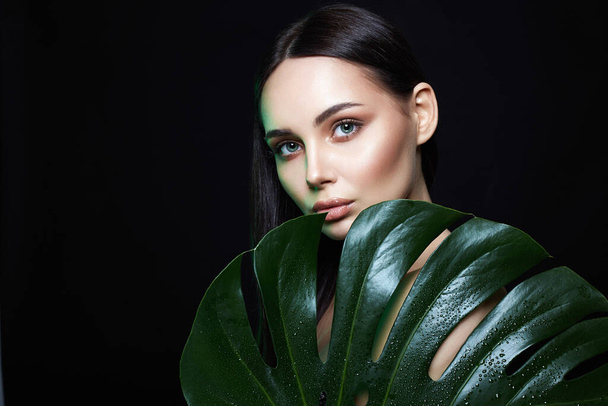 Beauty Portrait of beautiful girl in palm leaves. Brunette young woman with Make-up. Natural cosmetics concept - Photo, Image