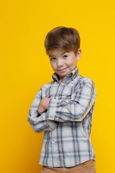 Cute little smiling boy in a tuxedo shirt with arms crossed on his chest Isolated on a yellow background. - Фото, изображение