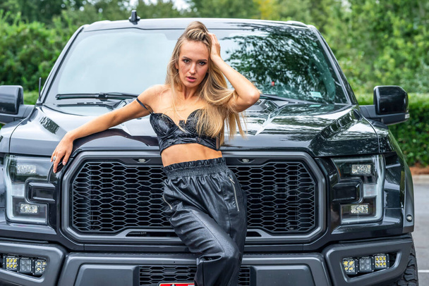 Uma linda modelo loira posa com um caminhão preto em um dia de outono - Foto, Imagem