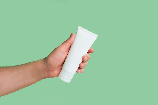 Mockup of unbranded white bottle tube for branding and label and male hand on a green background. Shaving foam or male skin care concept. Minimalism. - Zdjęcie, obraz