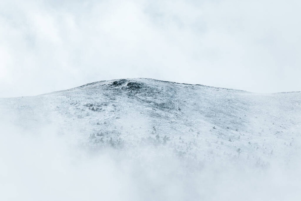 Verschneiter Gipfel eines weißen Berges mit Nebel und Schnee. Konzept von Kälte und Winter. Unübersichtlicher weißer Raum. - Foto, Bild