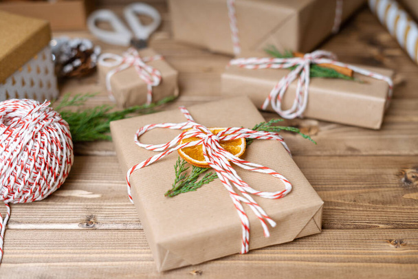 Wrapping Christmas gift, close up. Unprepared presents on wooden background with orange, cinnamon, ribbon, scissors, spruce branch, decor elements and items, side view. New year DIY packing Concept - Foto, imagen