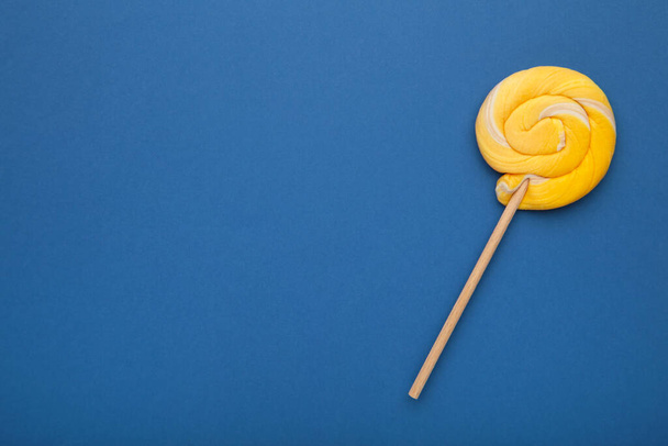 Yellow spiral lollipop on blue background. Top view - Zdjęcie, obraz