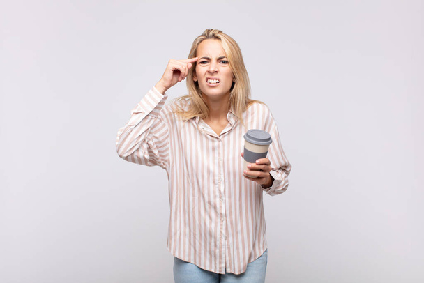 young woman with a coffee feeling confused and puzzled, showing you are insane, crazy or out of your mind - Foto, Imagen