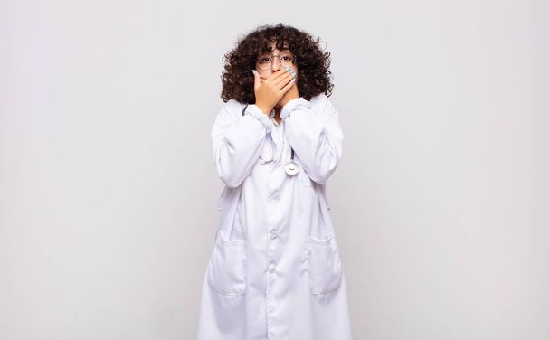 young woman physician covering mouth with hands with a shocked, surprised expression, keeping a secret or saying oops - Photo, Image