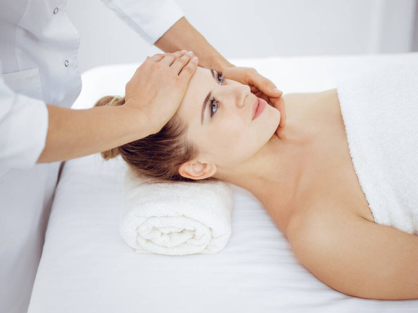 Young and blonde woman enjoying facial massage in spa salon. Beauty concept - Φωτογραφία, εικόνα