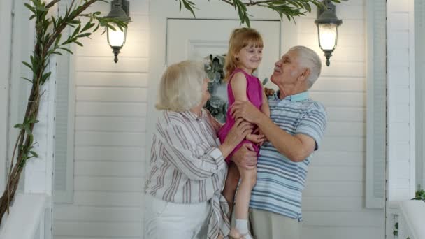 Šťastný starší dědeček a babička pár drží vnučku v rukou doma na verandě - Záběry, video