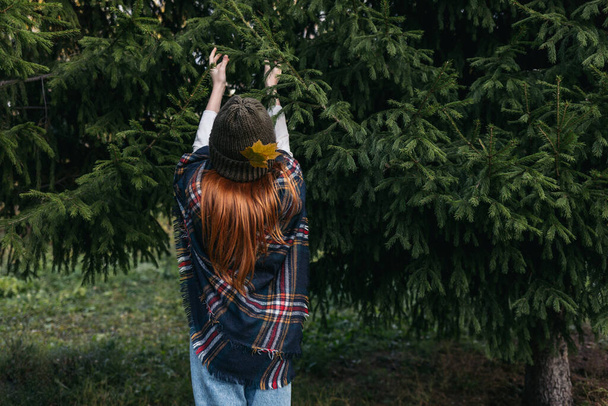 Рыжая девушка в вязаной шляпе, украшенной опавшими листьями. - Фото, изображение
