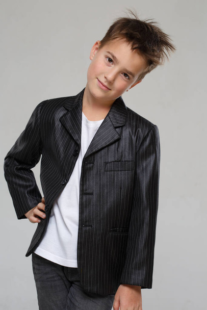 Little stylish smiling boy in jacket isolated on gray background. - Foto, afbeelding