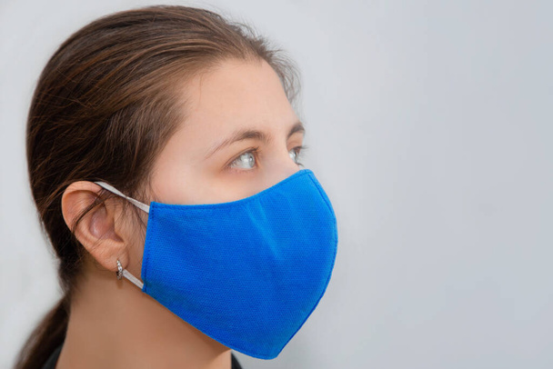 Portrait of a girl in a protective reusable mask of handwork isolated on a white background. The concept of a shortage of disposable medical masks in pharmacies and the popularity of reusable masks. - Photo, image