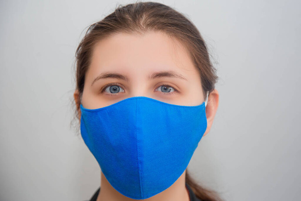 Portrait of a girl in a protective reusable mask of handwork isolated on a white background. The concept of a shortage of disposable medical masks in pharmacies and the popularity of reusable masks. - Photo, image