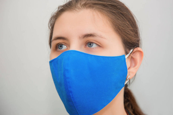 Portrait of a girl in a protective reusable mask of handwork isolated on a white background. The concept of a shortage of disposable medical masks in pharmacies and the popularity of reusable masks. - Фото, зображення