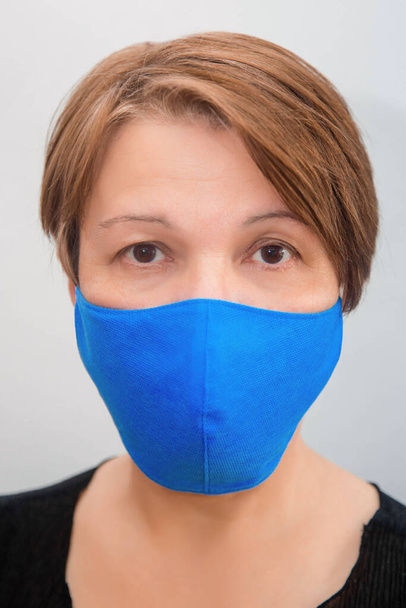 Portrait of a middle-aged woman in a protective reusable handmade mask on a white background. The concept of a shortage of disposable medical masks in pharmacies and the popularity of reusable masks. - Photo, image