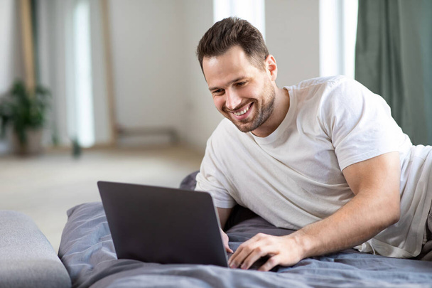 Щасливий фрілансер людина використовує ноутбук Робота онлайн брехня в ліжку
 - Фото, зображення