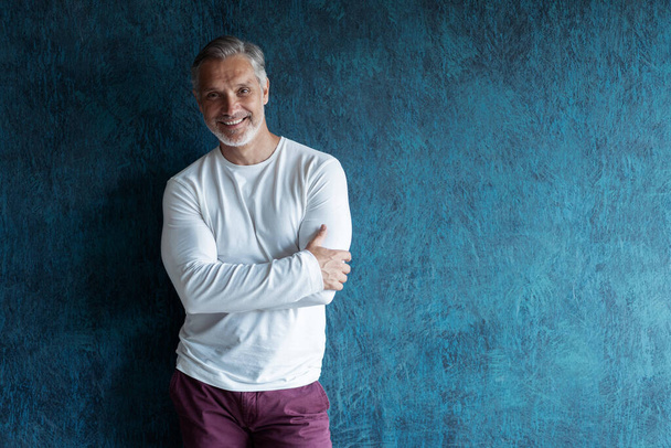 Casual Grey-haired Mature handsome man portrait over dark blue wall background. - 写真・画像