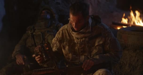 Soldier assembling gun near campfire - Záběry, video