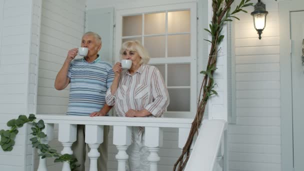 Oudere blanke echtpaar drinken koffie, omhelzen in de veranda thuis. Volwassen gelukkig gezin - Video