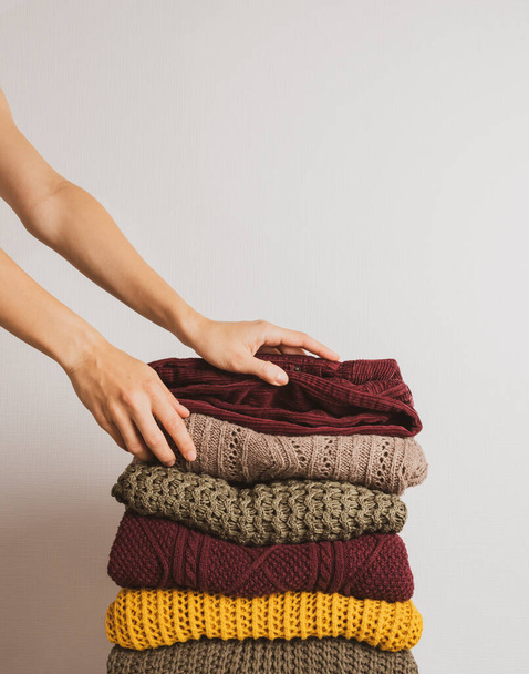 A woman takes a sweater from a stack of warm things on a white background. Faceless. Autumn color palette - 写真・画像