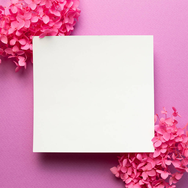 Almohadilla de notas en blanco, papel vacío con flores de hortensias rosas secas sobre fondo rosa. vista superior, espacio de copia - Foto, imagen