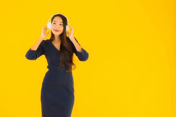 Retrato hermosa joven asiática mujer con auriculares para escuchar música en amarillo aislado fondo
 - Foto, imagen