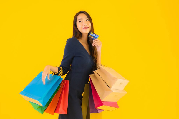 Retrato hermosa joven asiática mujer con bolsa de compras tarjeta de crédito y teléfono móvil inteligente amarillo aislado fondo
 - Foto, Imagen