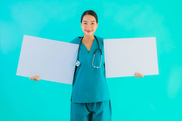 青い隔離された背景にコピースペースのための空の紙板紙と肖像画の美しい若いアジアの医師の女性-病院やクリニックのコンセプトのヘルスケア - 写真・画像