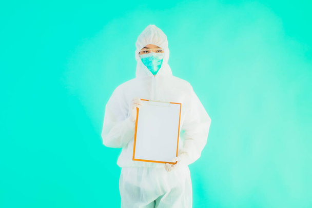 Retrato hermosa joven asiática médico mujer usar ppe o equipo de protección personal para proteger de coronavirus o covid19 con tarjeta vacía pizarra blanca sobre fondo aislado azul
 - Foto, imagen