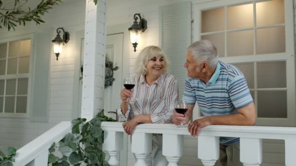Senior pareja de ancianos caucásicos beber vino en el porche en casa. Feliz familia jubilada madura descansando - Imágenes, Vídeo