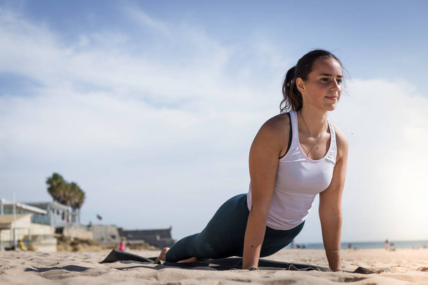 Mladá hravá žena dělá sportovní cvičení na pláži při západu slunce podél pobřeží Atlantského oceánu. Atraktivní Portugalka dělá jógu pózuje na pláži. Relaxační a meditační životní styl - Fotografie, Obrázek