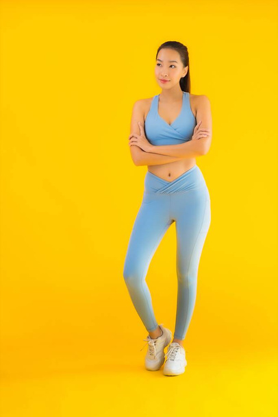 Retrato hermosa joven asiática deporte mujer con ropa deportiva listo para el ejercicio en amarillo aislado fondo
 - Foto, Imagen