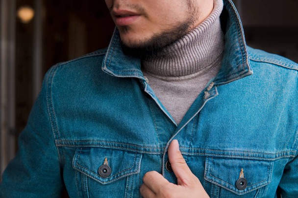 Young nice bearded man in jean jacket and roll-neck sweater at home. - Photo, Image
