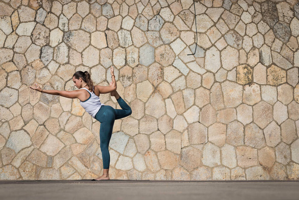 Silný učitel jógy žena dělá intenzivní cvičení podél pláže proti bezešvé vzor zeď. Mladá a atraktivní žena dělá jógu a pilates cvičení venku během čerstvého letního dne - Fotografie, Obrázek