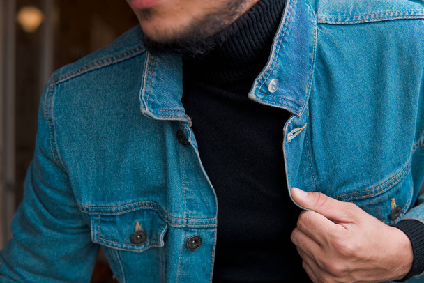Young nice bearded man in jean jacket and roll-neck sweater at home. - Photo, Image