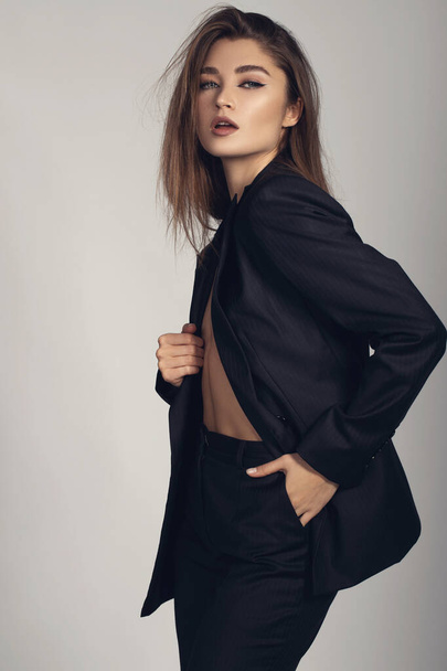 Fashion minimalist portrait of brunette female model on grey background. stylish clothing, black  classic style concept - Foto, afbeelding