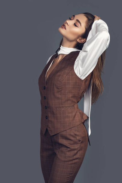 Fashion minimalist portrait of brunette female model on grey background. stylish clothing with scottish color, casual suit with women akcent  white silk shirt - Fotó, kép