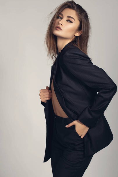 Retrato minimalista de moda de modelo feminino morena em fundo cinza. roupas elegantes, conceito de estilo clássico preto - Foto, Imagem