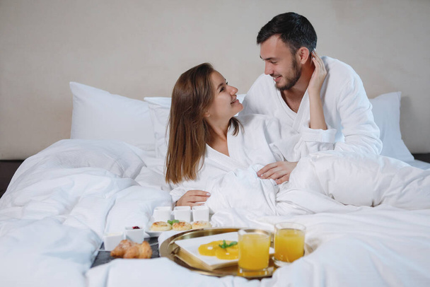 Bärtige Männer und eine Frau in weißen Mänteln frühstücken im Bett. Selektiver Fokus. - Foto, Bild