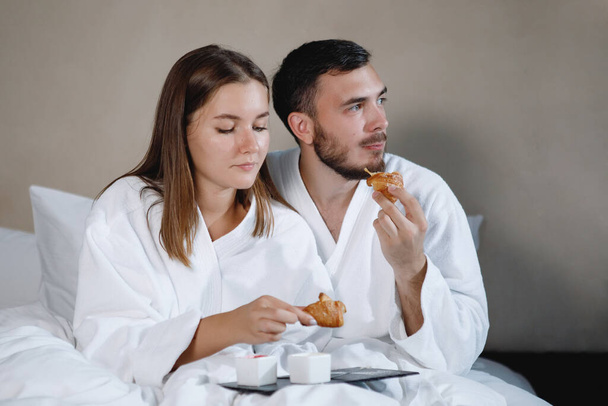 Brodaty mężczyzna i kobieta w białych fartuchach jedzą śniadanie w łóżku. Skupienie selektywne. - Zdjęcie, obraz