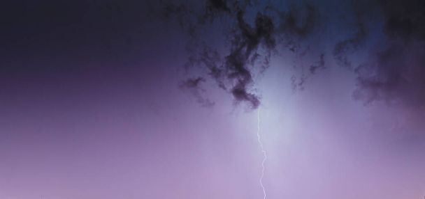Foto van een flits aan de nachtelijke hemel met gloeiende wolken in de zomer - Foto, afbeelding