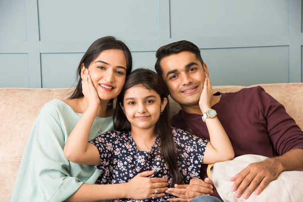 Retrato de la feliz familia joven asiática india mientras está sentada en el sofá, acostada en el suelo o sentada contra la pared - Foto, Imagen