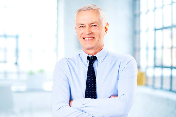 Portret uśmiechniętego starszego biznesmena w koszuli i krawacie, stojącego z rękami skrzyżowanymi w biurze.  - Zdjęcie, obraz