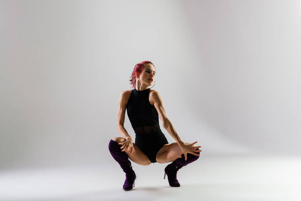 Fiatal, gyönyörű, rugalmas nő fekete kezeslábasban és magassarkúban pózol egy táncstúdióban.. - Fotó, kép