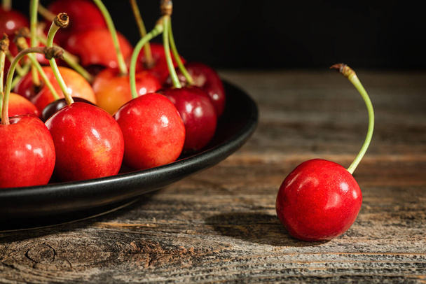 Sweet cherries on a plate on a wooden surface. Low key. - Photo, Image