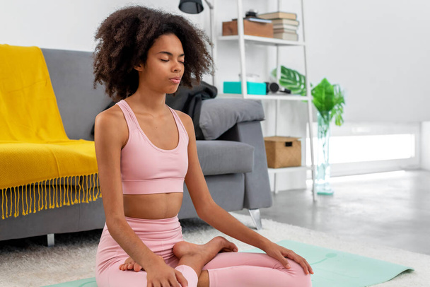 Afroamerikaanse vrouw het beoefenen van yoga lotus poseren voor meditatie in gezellig huis - Foto, afbeelding