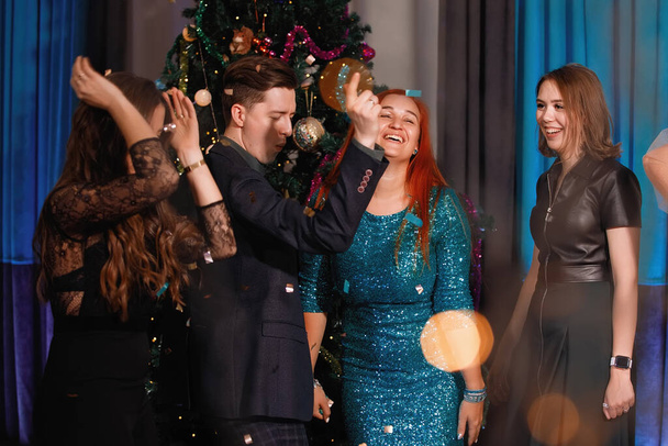 Eine Gruppe fröhlicher Freunde tanzt neben dem Weihnachtsbaum. Frauen lachen, jubeln. - Foto, Bild