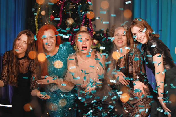 Il gruppo di amici festeggia il nuovo anno con coriandoli vicino all'albero di Natale. La gente ride e si rallegra. - Foto, immagini