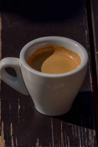 Kávésbögre a fa asztalon. Egy csésze forró eszpresszó kávé, arab főzet, textúra háttérrel. Fekete kávé fehér kerámia csésze fából készült asztalon - Fotó, kép