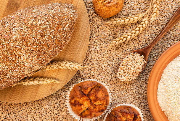 Csendélet kenyérrel, muffinnal, sütivel, tüskékkel, egy tányér tönkölyliszttel és egy kanállal tele gabonával.. - Fotó, kép