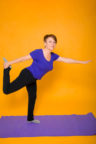 Woman at the age of doing yoga standing on a yellow background. - Foto, Imagen