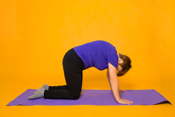 Aged woman doing yoga on a purple rug. Studio photo on a yellow background. - Fotografie, Obrázek
